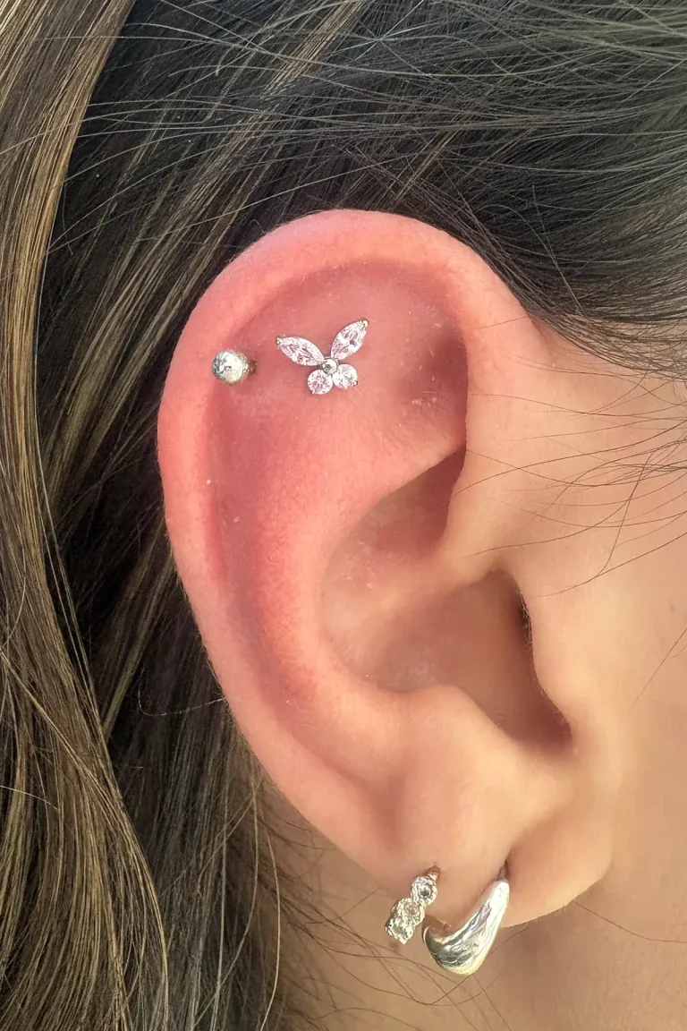 Piercing no helix com joia de borboleta cravejada e ponto de luz, com argolas no lóbulo, feito na Visão Tattoo em Curitiba