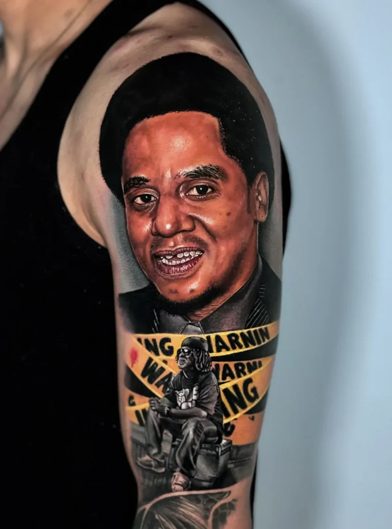 Tatuagem realista no braço: retrato em homenagem com faixas amarelas de aviso e figura em preto e cinza, feita no estúdio Visão Tattoo, em Curitiba