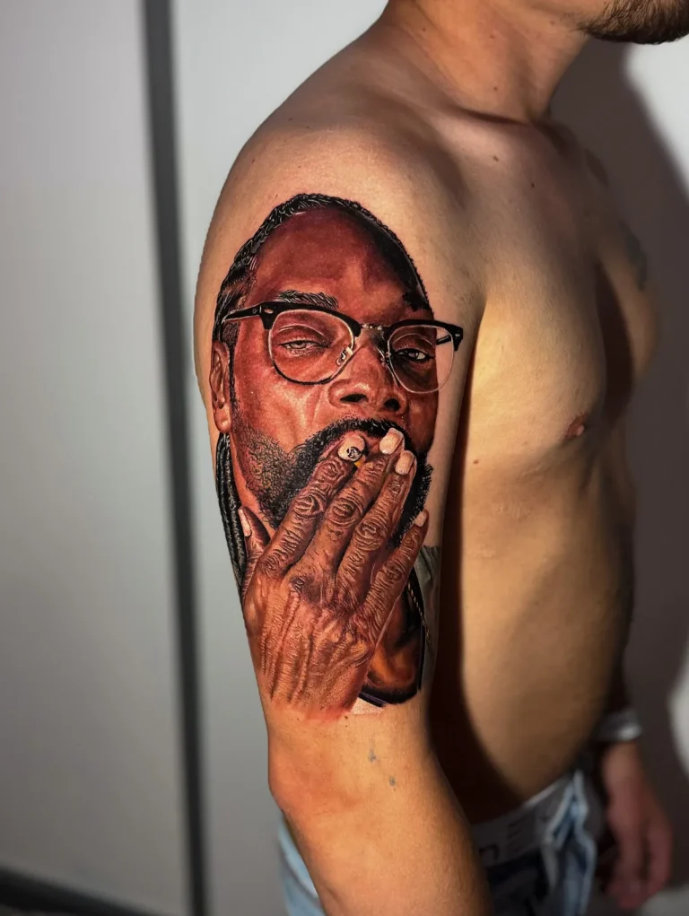Tatuagem realista no braço: retrato de homem de óculos e tranças com a mão no rosto, em tons de marrom, feita no estúdio Visão Tattoo, em Curitiba