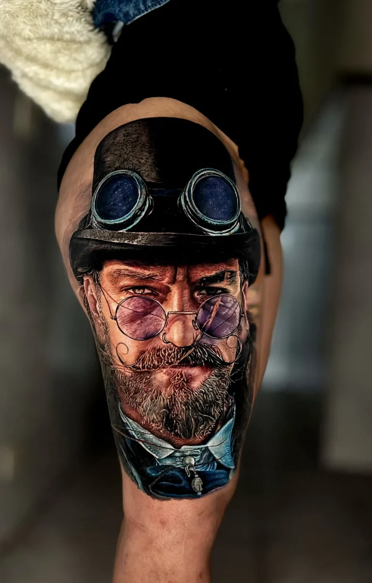Tatuagem realista colorida na coxa: retrato de homem com chapéu-coco, óculos de aviador e óculos redondos lilás, estilo steampunk, feita na Visão Tattoo em Curitiba