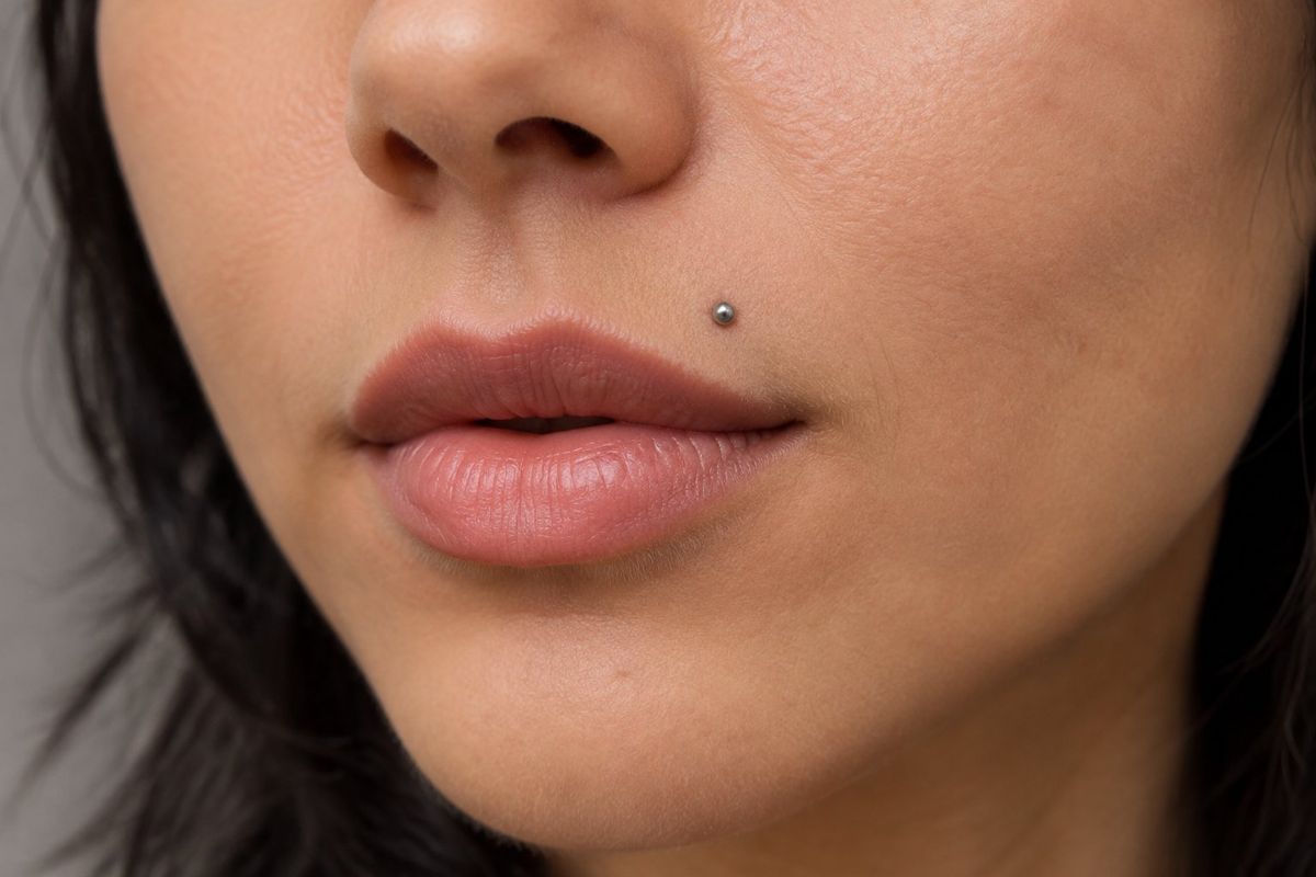 Piercing Monroe: Guia Completo Sobre Cuidados, Dor e Cicatrização Pessoa com um pequeno piercing acima do lado esquerdo do lábio superior.